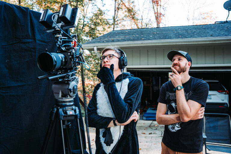 Ian Hoyt in a skunk costume and headphones, watching a take beside the camera